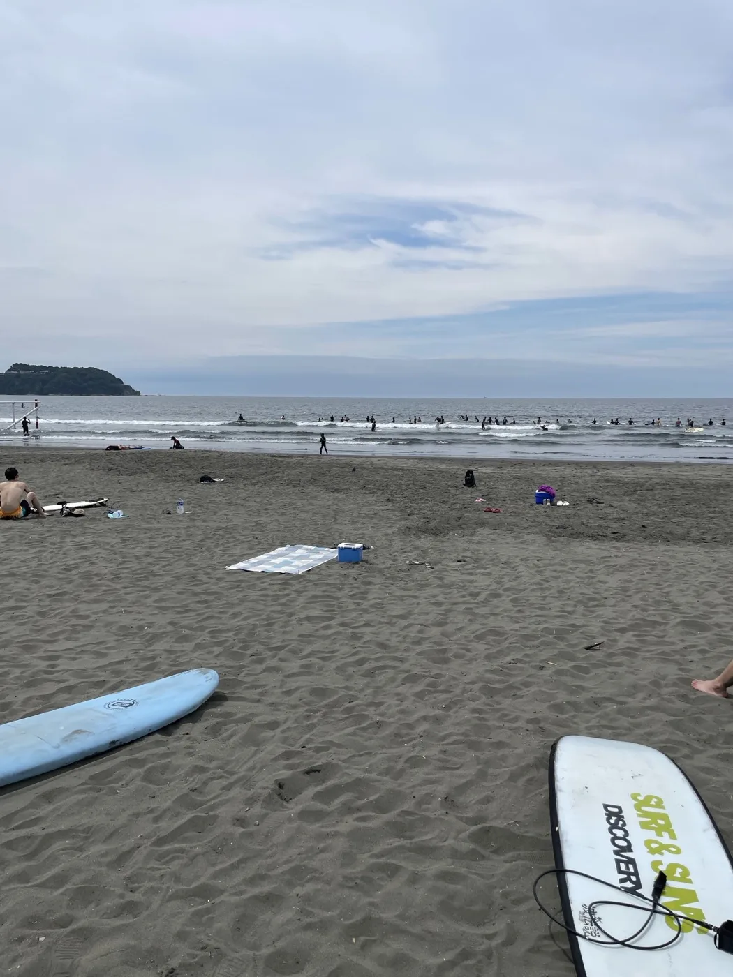 鵠沼海岸の砂浜に並ぶレンタルのソフトボードと、沖でサーフィンする人たち